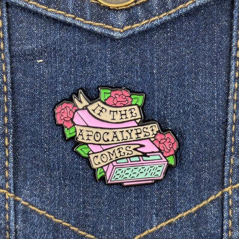 May include: A pink and black enamel pin with the text "IF THE APOCALYPSE COMES" on a banner, surrounded by pink roses and green leaves. The pin is in the shape of a retro digital clock.
