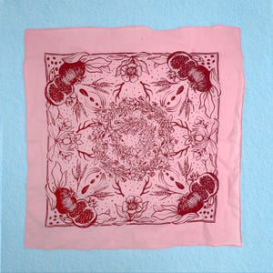 May include: Pink bandana with a red floral pattern featuring pomegranates and other botanical elements. The bandana is a square shape with a fringed edge.