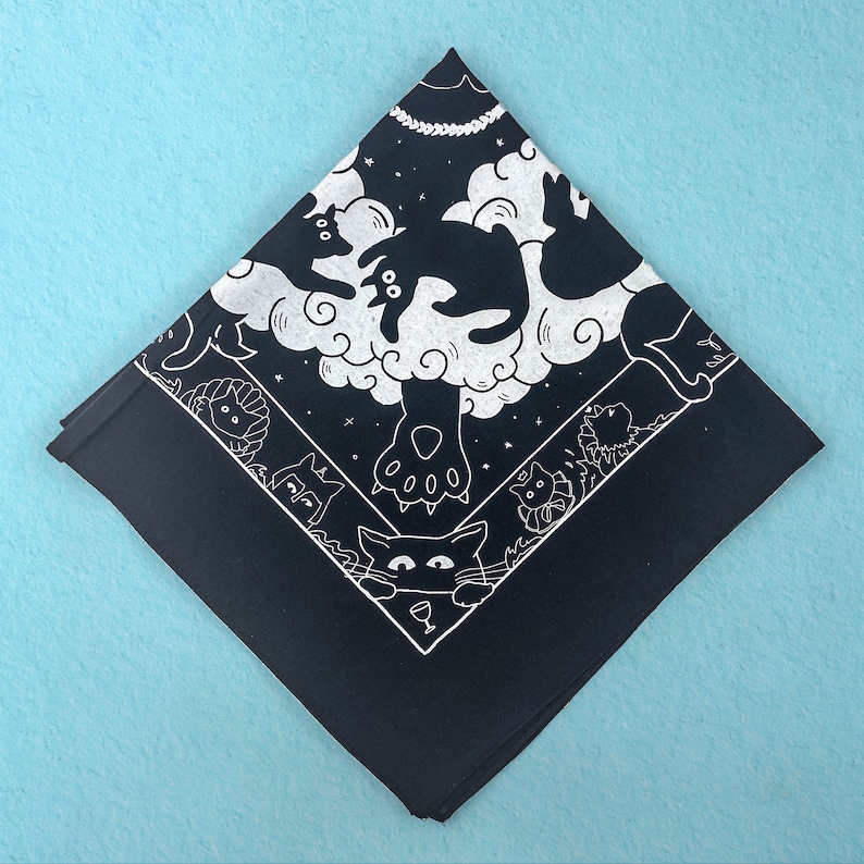 Puede incluir: Bandana negra con un dise&ntilde;o blanco de gatos y nubes. Los gatos est&aacute;n en varias poses, incluyendo dormir, jugar y mirar hacia arriba a las nubes. La bandana est&aacute; hecha de algod&oacute;n y mide aproximadamente 56 cm cuadrados.