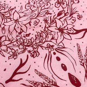 May include: A pink fabric with a red floral pattern. The pattern includes flowers, leaves, and wheat stalks.