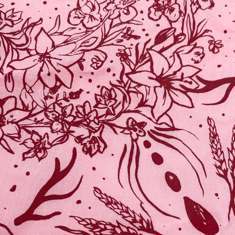 May include: A pink fabric with a red floral pattern. The pattern includes flowers, leaves, and wheat stalks.