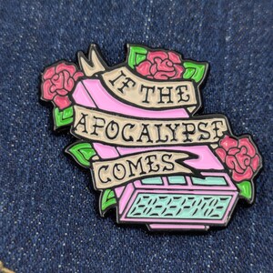 May include: A pink and black enamel pin with the text "IF THE APOCALYPSE COMES" on a banner, surrounded by pink roses and green leaves. The pin features a retro-style digital clock display.