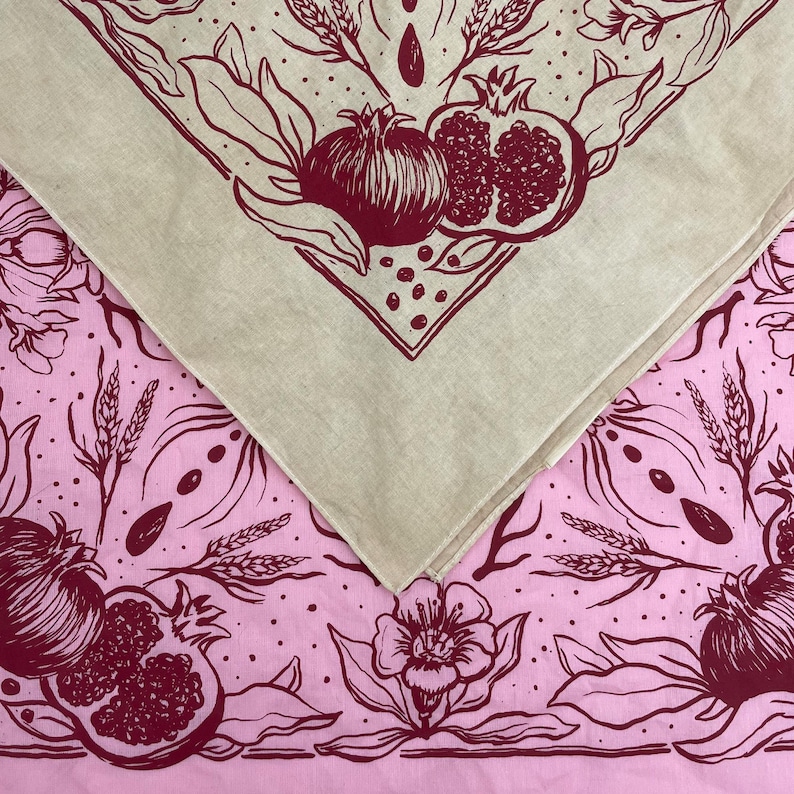 May include: Two fabric squares with a pink and white floral pattern and a beige square with a red pomegranate pattern. The fabric squares are sewn together to create a larger square.
