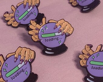 May include: Four purple and green enamel pins with a design of a crystal ball with hands around it. The crystal ball has a green progress bar inside and the text "loading..." underneath.