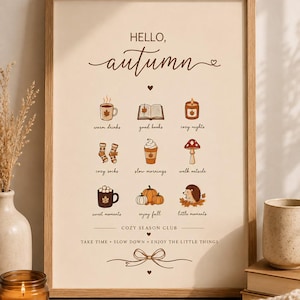 May include: A framed wall art print with a cream background featuring the text HELLO, autumn at the top. Below are nine small illustrations with labels: warm drinks, good books, cozy nights, cozy socks, slow mornings, walk outside, sweet moments, enjoy fall, and little moments. The bottom text reads COZY SEASON CLUB and TAKE TIME, SLOW DOWN, ENJOY THE LITTLE THINGS.