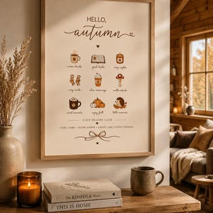 May include: A framed wall art print with a cream background featuring the text HELLO, autumn and a grid of nine small illustrations including a mug, book, candle, socks, coffee, mushroom, cocoa, pumpkins, and hedgehog with the text COZY SEASON CLUB.