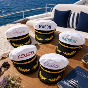 May include: Five white and black captain hats with gold braided trim and yellow embroidered laurel leaves on the brim. Each hat features a personalized name embroidered in different colors: Harper, Mason, Madison, Alexander, and Charlotte.