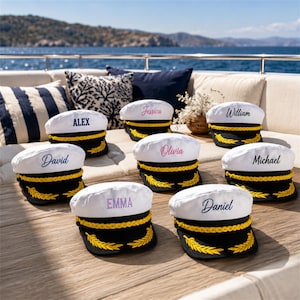 May include: A collection of white captain hats with black brims, each featuring a gold braided cord and embroidered gold laurel leaves. The hats are personalized with names including Alex, Jessica, William, David, Olivia, Michael, Emma, and Daniel.