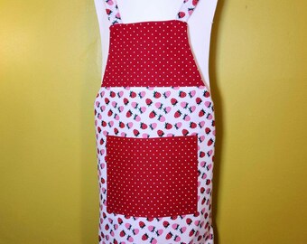 May include: A kitchen apron featuring a red and white polka dot bib and a matching central pocket. The main body of the apron displays a white background patterned with small red strawberries and green leaves, complemented by matching shoulder straps.