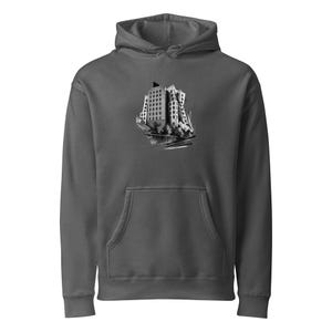 May include: A charcoal gray hooded sweatshirt featuring a central graphic print of a multi-story building with a distorted, angular architectural design. The illustration is rendered in shades of black, white, and gray, showing windows and structural details.