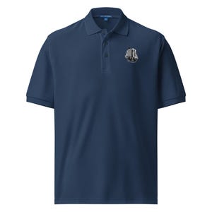 May include: A navy blue short-sleeve polo shirt with a collar and a three-button placket. On the left chest, there is a small, detailed black and white graphic illustration of a multi-story building with architectural features.