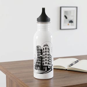 May include: A white stainless steel water bottle with a black screw-top lid. The bottle features a black and white graphic illustration of a modern, curved architectural building with geometric lines and patterns printed on the front surface.
