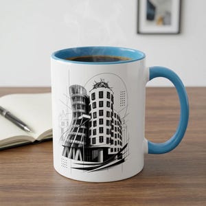 May include: A white ceramic mug with a bright blue interior and handle, featuring a black and white architectural line drawing of the Dancing House in Prague. The design includes geometric patterns, thin lines, and a circular graphic element.