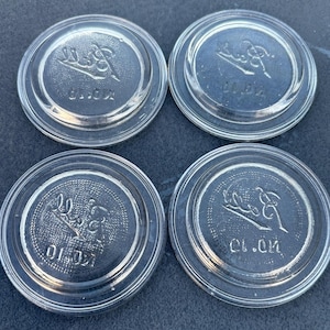 May include: Four circular clear glass lids for jars, each featuring a raised embossed logo that reads Ball and the text NO. 10. The lids have a smooth, flat top surface with a slightly raised outer rim and a textured underside design.