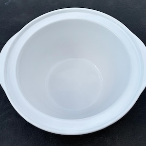 May include: A round, white ceramic serving bowl with a smooth, glossy finish and integrated side handles. The bowl features a wide, open top and a deep, curved basin, presenting a clean, uniform appearance throughout the entire interior surface.