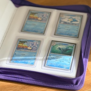 Op de afbeelding: Een paarse verzamelkaartenmap met ritssluiting en doorzichtige plastic hoezen met vier rechthoekige spelkaarten. Elke kaart is voorzien van blauwachtige illustraties en Japanse tekst op de voorzijde van de kaarten.