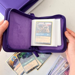 Pode incluir: Um fichário roxo para cartas colecionáveis com zíper e forro interno macio, contendo uma coleção de cartas de jogo. Uma carta com a personagem Cruella d'Enfer está visível dentro do fichário, com outras cartas espalhadas abaixo.