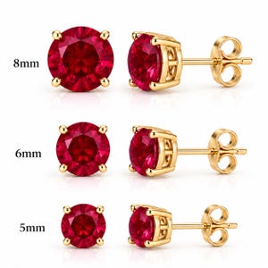 May include: Three pairs of round, deep red stud earrings set in gold-toned metal prongs. The earrings are displayed in three sizes: 8mm, 6mm, and 5mm, with each pair shown from both a front-facing view and a side profile view featuring the post back.