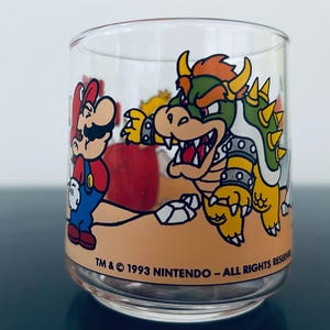 Pode incluir: Um copo transparente com um gráfico colorido do Mario e do Bowser da franquia Super Mario. A base do design inclui o texto TM & © 1993 NINTENDO – ALL RIGHTS RESERVED impresso em preto ao longo da borda inferior do copo.