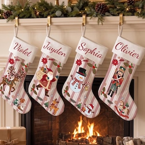 May include: Four Christmas stockings with white cuffs featuring the names Violet, Jayden, Sophia, and Olivier in red script. The stockings have a pink and white striped pattern with festive graphics including a reindeer, Santa Claus, a snowman, and a nutcracker.