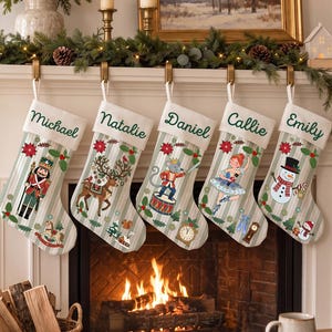 May include: Five personalised Christmas stockings with a light grey and white striped pattern. Each stocking features a white cuff embroidered with the names Michael, Natalie, Daniel, Callie, and Emily, and displays festive holiday illustrations.