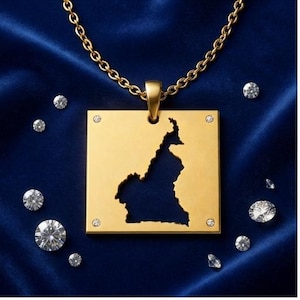May include: A gold-toned square pendant necklace featuring a cutout of the map of Cameroon. The pendant is suspended from a matching gold-toned chain and is accented with four small, clear, round-cut stones set at each of the four corners.