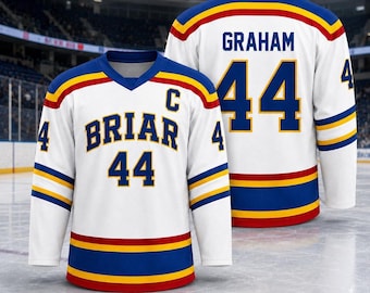 May include: A white hockey jersey featuring blue, yellow, and red stripes on the sleeves and hem. The front displays the text BRIAR, the number 44, and a C patch. The back shows the name GRAHAM and the number 44 in blue lettering.