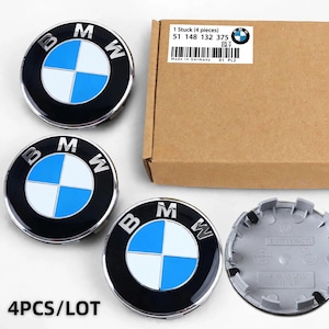 May include: A set of four circular BMW wheel center caps featuring the iconic blue, white, and black logo. The caps are displayed alongside a brown cardboard box labeled with the text 1 Stuck 4 pieces 51 148 132 375 Made in Germany.