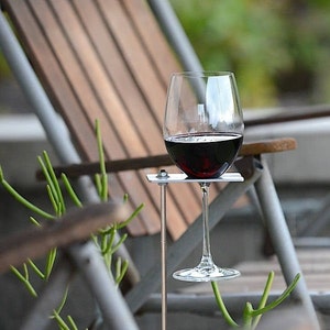 May include: A metal wine glass holder with a glass of red wine. The holder is attached to a metal rod that is inserted into the ground.