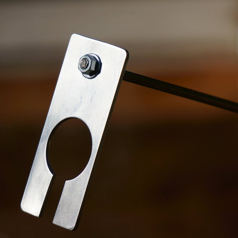 May include: A silver metal bracket with a round hole and a screw. The bracket is attached to a metal rod.