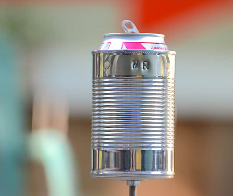 Puede incluir: Una lata de metal reutilizada con una tapa de leng&uuml;eta, transformada en un objeto decorativo. El exterior plateado de la lata es acanalado y la parte superior presenta detalles en rosa y blanco. Las iniciales "MR" est&aacute;n estampadas en el lateral.