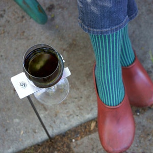 May include: A metal wine glass holder with a glass of red wine. The holder is attached to a metal stake that is inserted into the ground. The holder is designed to keep the wine glass upright and secure.