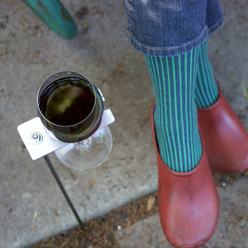 May include: A metal wine glass holder with a glass of red wine. The holder is attached to a metal stake that is inserted into the ground. The holder is designed to keep the wine glass upright and secure.