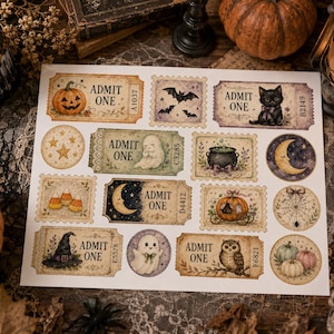 May include: A white sheet of paper featuring various Halloween-themed stickers, including rectangular tickets labeled ADMIT ONE with illustrations of a pumpkin, a black cat, a ghost, a cauldron, a witch hat, and an owl, plus circular moon and spiderweb designs.