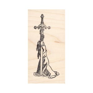 May include: A black and white illustration of a sword being pulled from a stone. The sword has a decorative hilt and is wrapped in a ribbon.