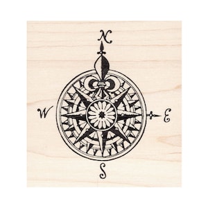 May include: A black compass rose design with directional indicators (N, S, E, W) and a fleur-de-lis at the top, printed on a light wood grain background. The compass rose features a detailed starburst pattern.