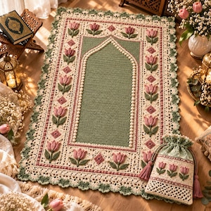 May include: A rectangular crochet prayer rug featuring a central sage green mihrab design bordered by cream-colored yarn with pink tulip motifs and green leaves. The edges are finished with a scalloped lace border, accompanied by a matching drawstring pouch.