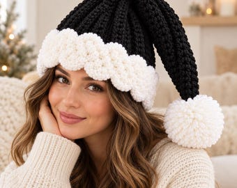 May include: A black crocheted hat with a thick, white, textured brim and a large white pom-pom at the tip. The hat features a ribbed stitch pattern throughout the black section, creating a distinct contrast with the soft, white, scalloped-edge trim.