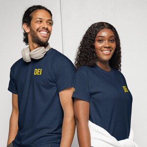 May include: A navy blue short-sleeved t-shirt featuring the letters DEI printed in yellow on the upper left chest. The shirt has a crew neckline and a standard fit. The fabric is a solid dark blue color with a smooth texture and clean finish.