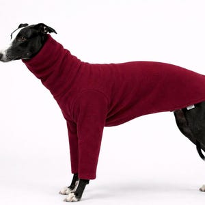 May include: A black and white dog wearing a burgundy fleece dog sweater with a high turtleneck collar and long sleeves. The dog is standing on a white background, showcasing the sweater's fit and design.