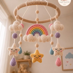 May include: A crochet baby mobile featuring a circular beige frame with hanging elements including a central rainbow, three smiling stars in cream and yellow, purple and blue teardrop shapes, and small round beads suspended by white cords.