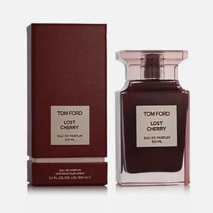 Op de afbeelding: Een Tom Ford Lost Cherry eau de parfum sprayfles en de bijbehorende rechthoekige doos. Zowel de donkerbordeauxrode fles als de getextureerde doos hebben een wit label met de tekst Tom Ford Lost Cherry Eau de Parfum 100 ml.