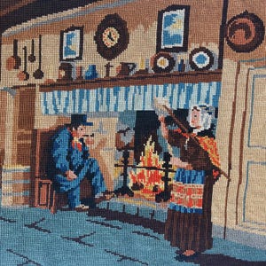 Puede incluir: Un tapiz de punto de aguja que representa una escena interior con una persona con traje azul sentada junto a una chimenea y otra con vestido marrón de pie. La habitación cuenta con una repisa con cuadros, un reloj y utensilios colgados.