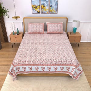 May include: A bed featuring a light-colored wooden frame and a mattress covered in a white bedsheet with a repeating red floral pattern. Two matching rectangular pillows with the same red floral print are placed against the headboard.