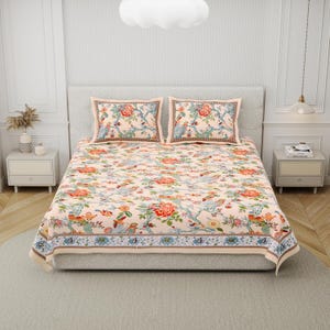 May include: A bed set featuring a light peach-colored bedspread and two matching rectangular pillowcases. The fabric displays a repeating pattern of colorful birds, blooming flowers, and leafy branches, finished with a decorative blue border.