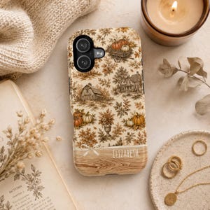 May include: A phone case featuring a cream-colored background with a repeating pattern of brown and orange pumpkins, autumn leaves, and rural buildings. The bottom section has a wood grain texture with a white bow and the name ELIZABETH printed.