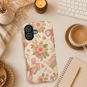 May include: A smartphone case featuring a cream-colored background with a repeating pattern of pink flowers, green leaves, pink ribbons, and small checkered squares in shades of pink and green. The case has a black camera cutout at the top left corner.