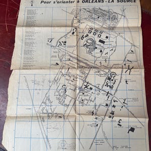以下が含まれることがあります： Pour s'orienter à ORLÉANS - LA SOURCEと題されたヴィンテージの紙の地図。クリーム色の背景に青いグリッドが重ねられ、黒い線画で街のレイアウトが描かれています。地図には方位磁針、通りの名前、建物のラベルが含まれています。