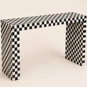 May include: A rectangular console table featuring a continuous black and white chequered pattern across its entire surface. The furniture piece has a flat top and two vertical side panels, creating a clean, geometric, and open-frame structure.