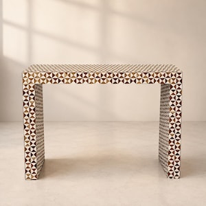 May include: A rectangular console table featuring a repeating geometric pattern of brown and white triangles across its entire surface. The table has a waterfall design with two vertical side panels and a flat top, creating a continuous structure.